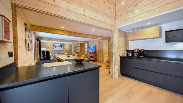 Une cuisine moderne dotée d’un îlot central, de meubles de couleur sombre et d’un mur d’accent en pierre.