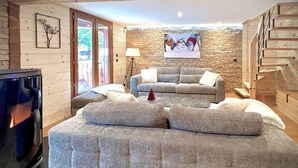 Un salon chaleureux avec un mur en pierre, un canapé gris, une petite table et un escalier.