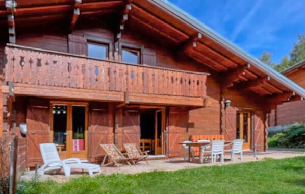 Una cabaña de madera con balcón, mobiliario exterior y un césped bien cuidado.