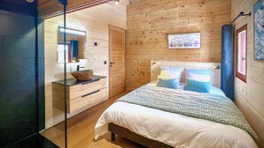 Une chambre dans une cabane en bois, avec un lit, une table de chevet en bois, un miroir et une fenêtre.