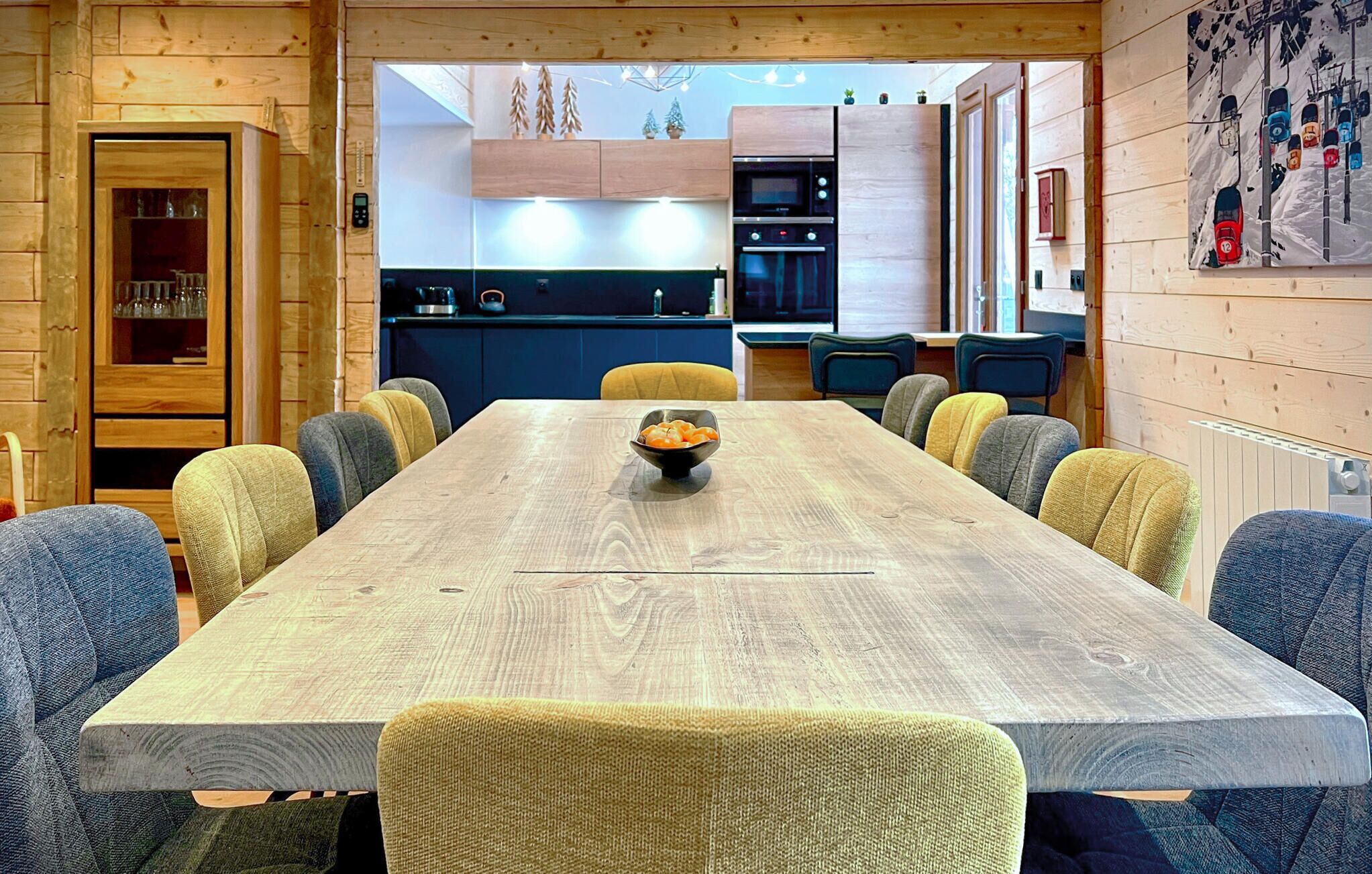 A wooden dining room with a long table, chairs, and a bowl of fruit.