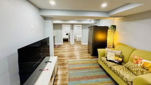 A modern living room with a flat-screen TV, a sofa, a refrigerator, and a striped rug.