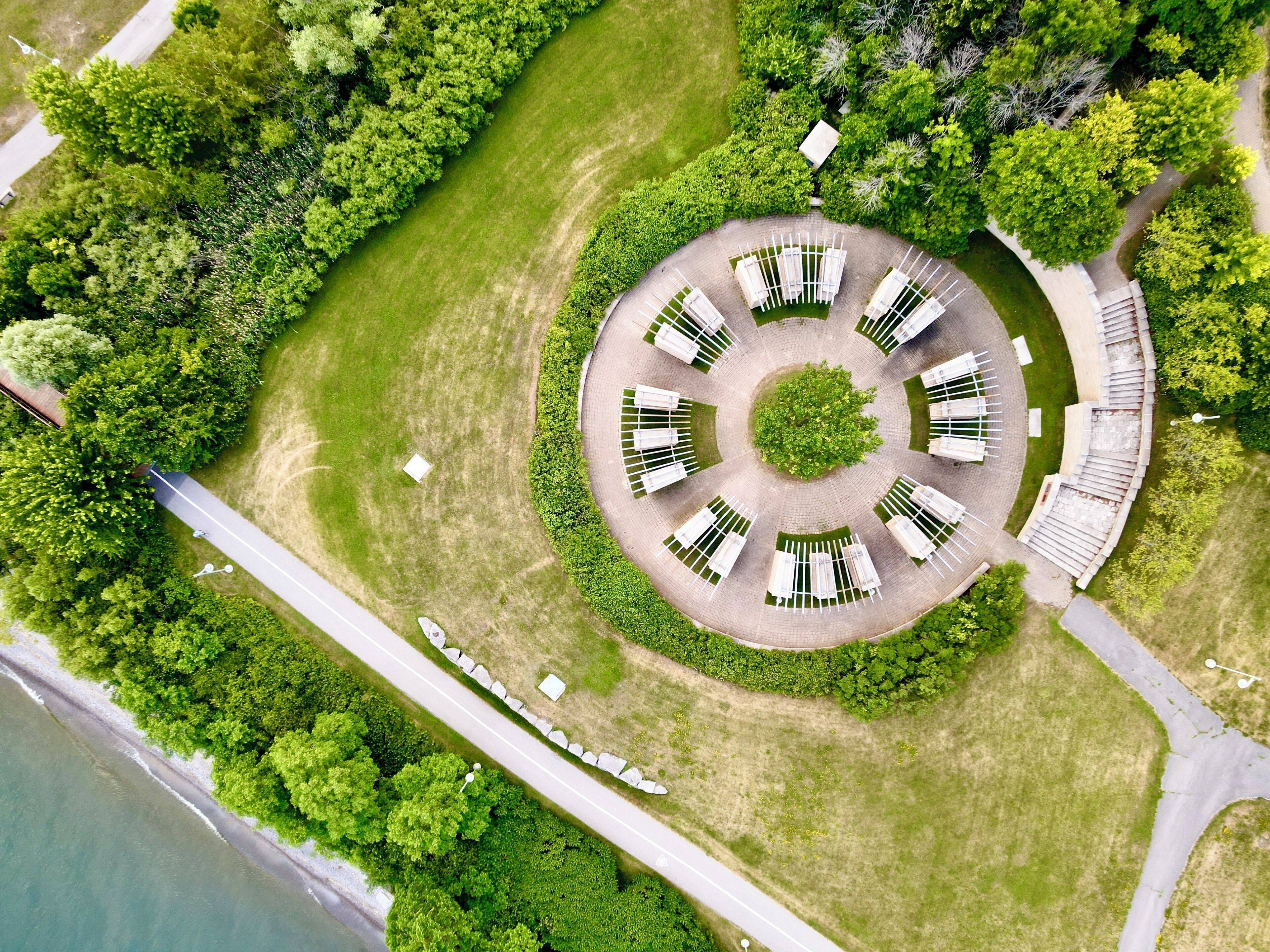 Vue aérienne d’un espace extérieur circulaire aménagé en coin salon, avec des bancs blancs, entouré d’une végétation luxuriante et bordé d’un chemin pavé.