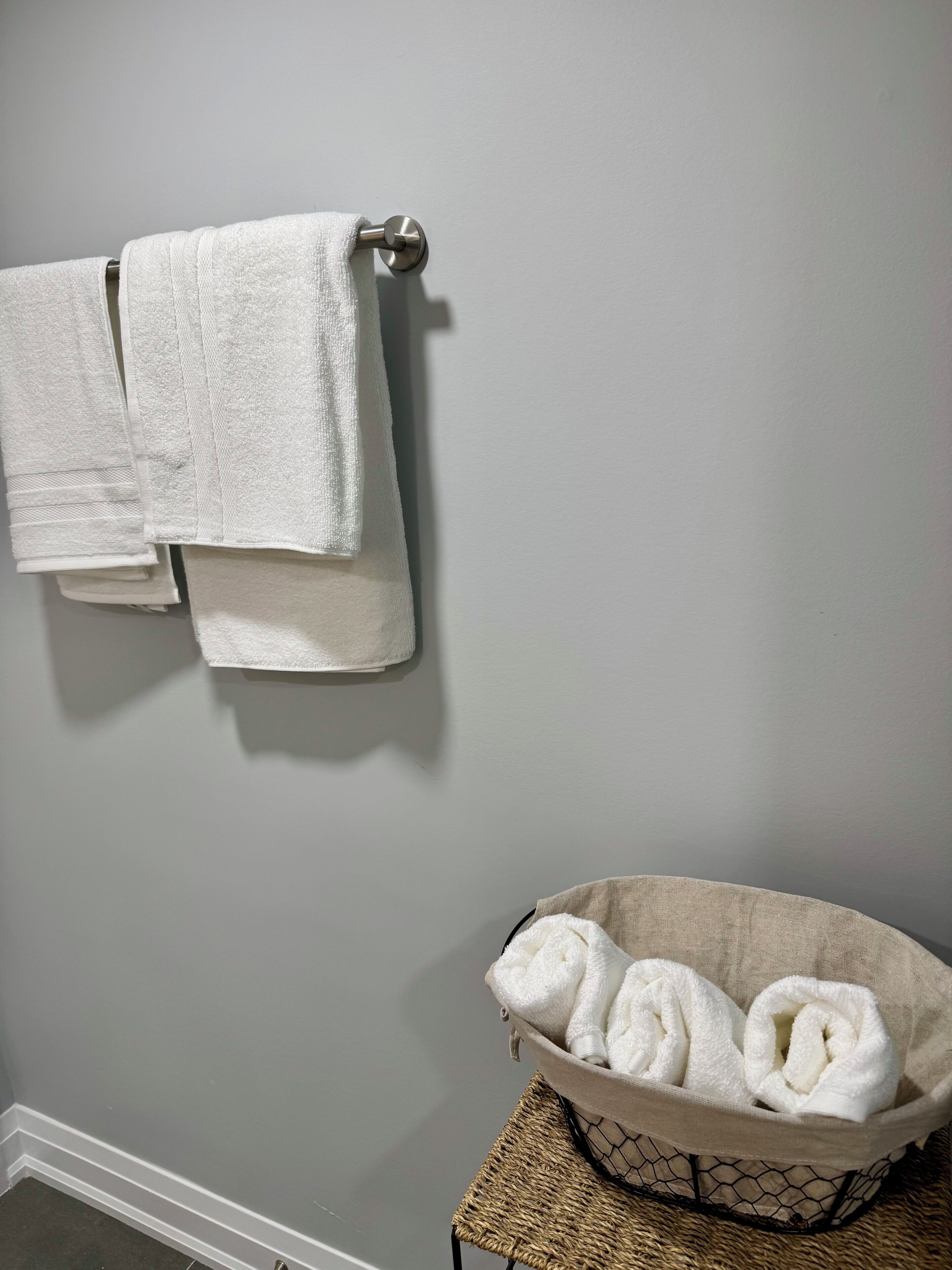 Een badkamer met een handdoekrek met twee handdoeken en een geweven mand met opgerolde handdoeken.