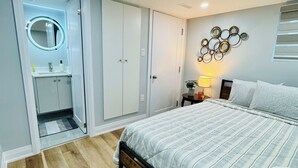 A bedroom with a bed, a bedside table, a nightstand, a mirror, a wardrobe, and a wall-mounted light fixture.