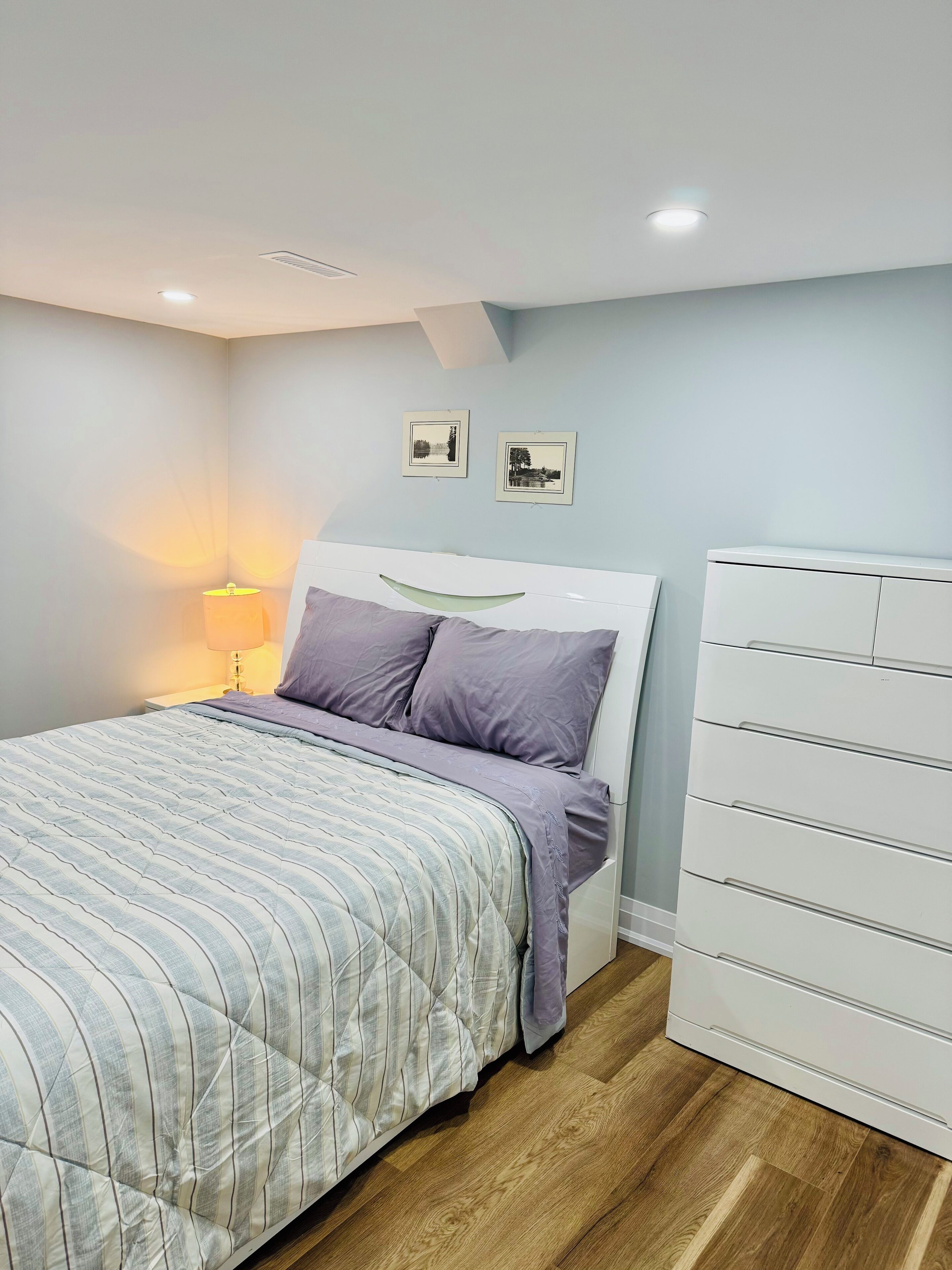 A bedroom with a bed, a nightstand with a lamp, and a dresser.