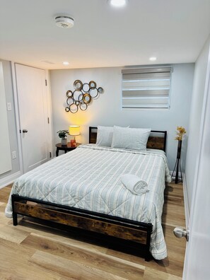 Een slaapkamer met een bed, een rond decoratiestuk aan de muur, een bedlampje en een raam met jaloezieën.