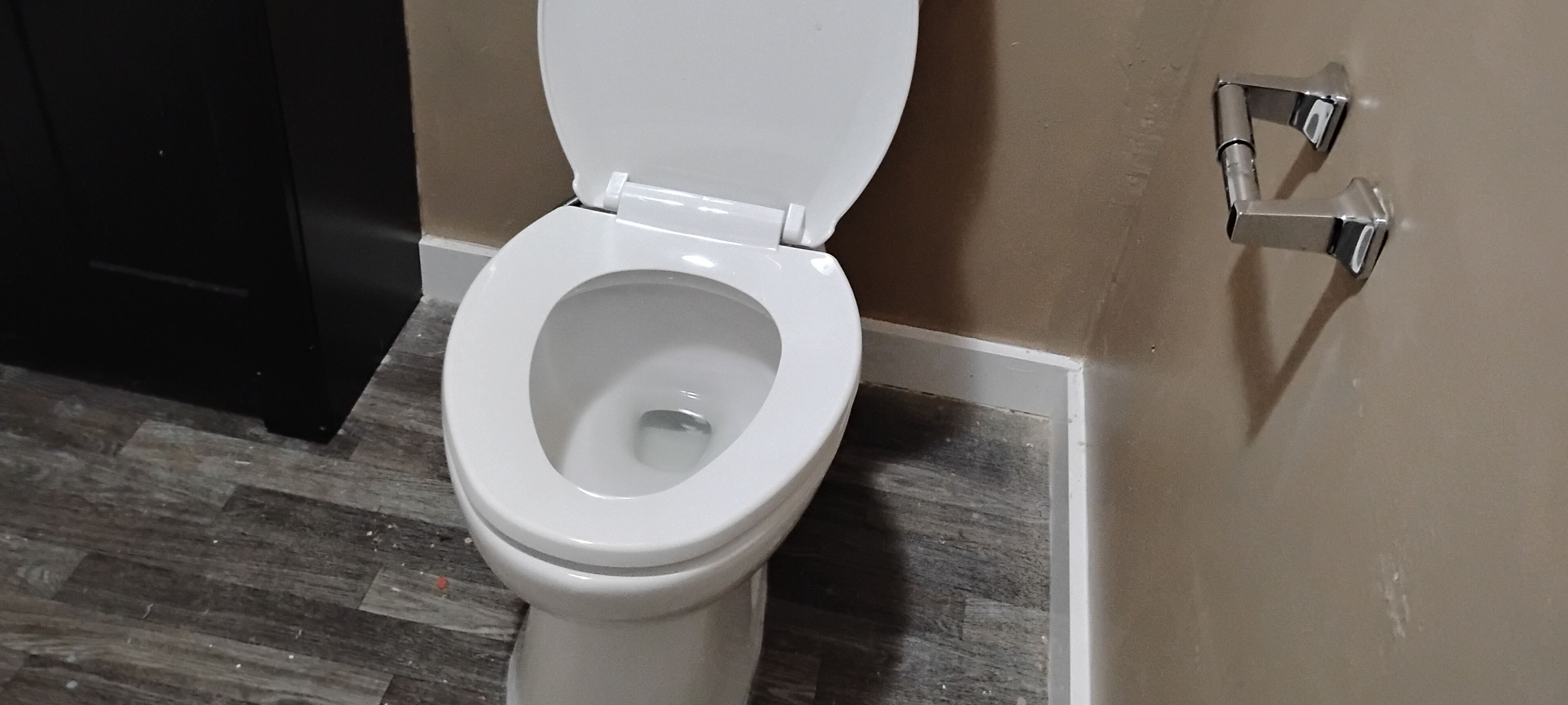 A toilet with a closed lid in a bathroom with wooden flooring and beige walls.