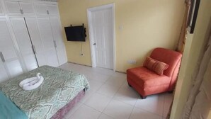 A bedroom with a bed, a wardrobe, a red chair, and a television on the wall. - Union Hilltop Paradise Villas - Premium Poolside Villa with Scenic Views (Castries)