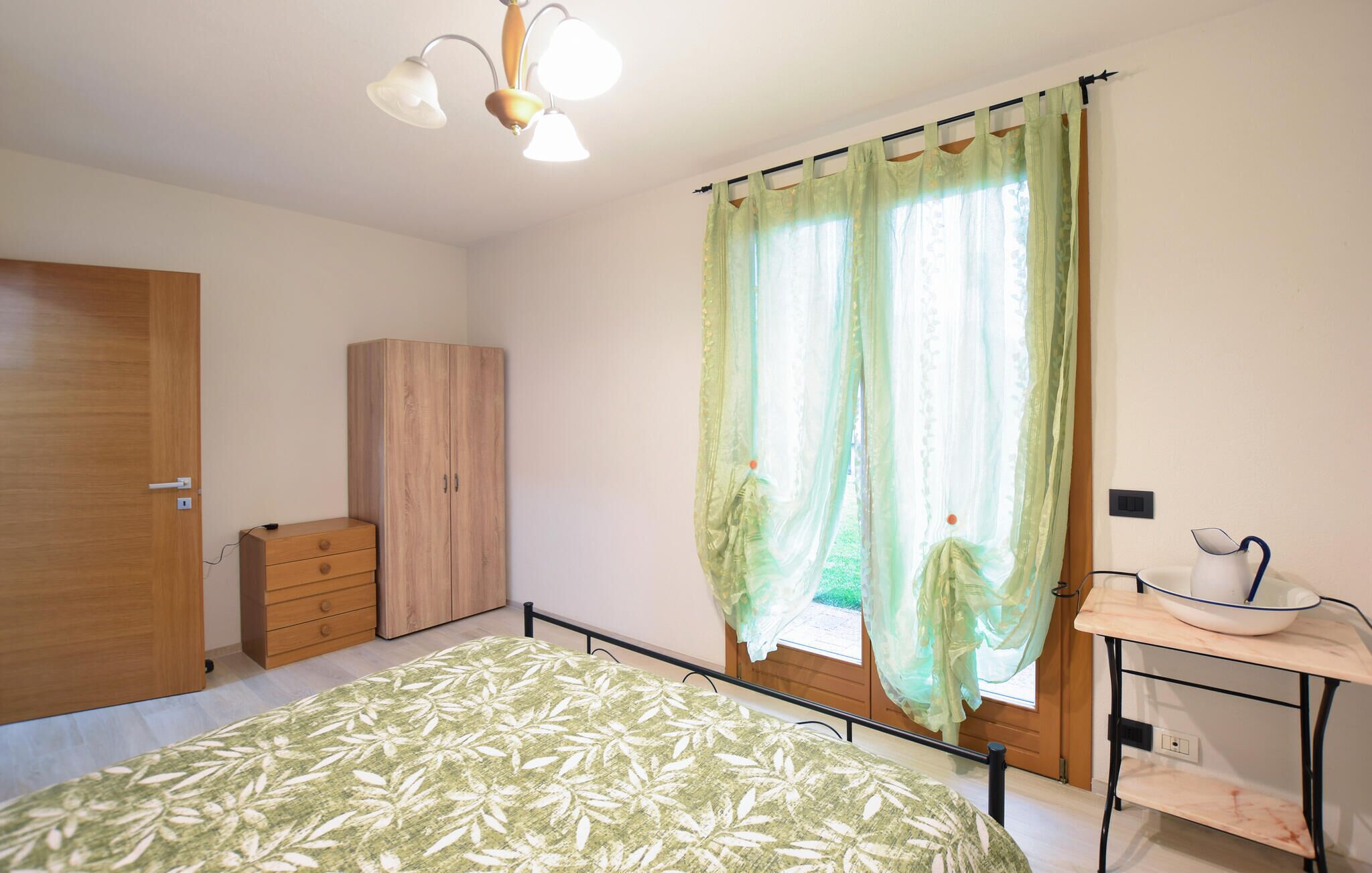 A bedroom with a bed, a wardrobe, a desk with a chair, and a window with curtains.