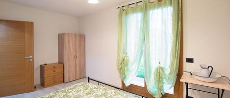 A bedroom with a bed, a wardrobe, a desk with a chair, and a window with curtains.