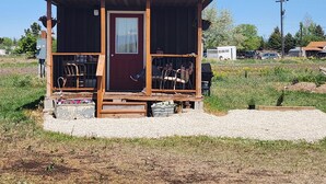 Una pequeña cabaña de madera con techo rojo, una puerta principal y un porche con dos sillas.