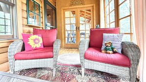 Ein gemütliches Blockhäuschen-Interieur mit Korbmöbeln, einem gemusterten Teppich und einem Teddybären auf einem Stuhl.