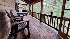 Eine Holzterrasse mit überdachtem Bereich, Gartenmöbeln und Blick auf Bäume.