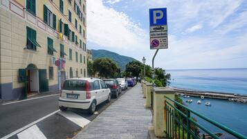 Eine Küstenstraße mit parkenden Autos, einem blauen Parkschild und Blick auf das Meer.