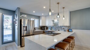 A modern kitchen with a large island, stainless steel appliances, pendant lighting, and a view of the street. - Run Away Bay 181 by SeaBreeze Vacation (Bradenton Beach)