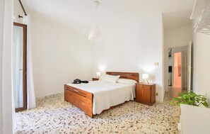 Ein Schlafzimmer mit einem hölzernen Bett, zwei Nachttischen mit Lampen, einem Spiegel und einer mit Vorhängen versehenen Tür.