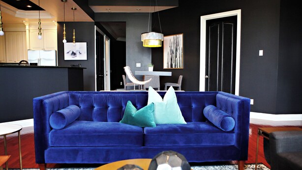A modern living room with a blue sofa, two soccer balls on a round table, and a kitchen area in the background.