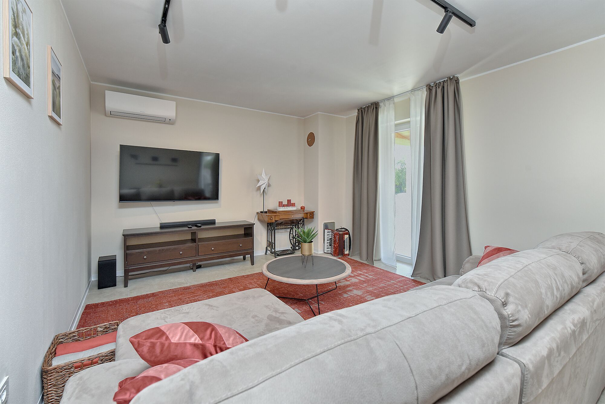 A living room with a sofa, a TV, a small table, and a window with curtains.