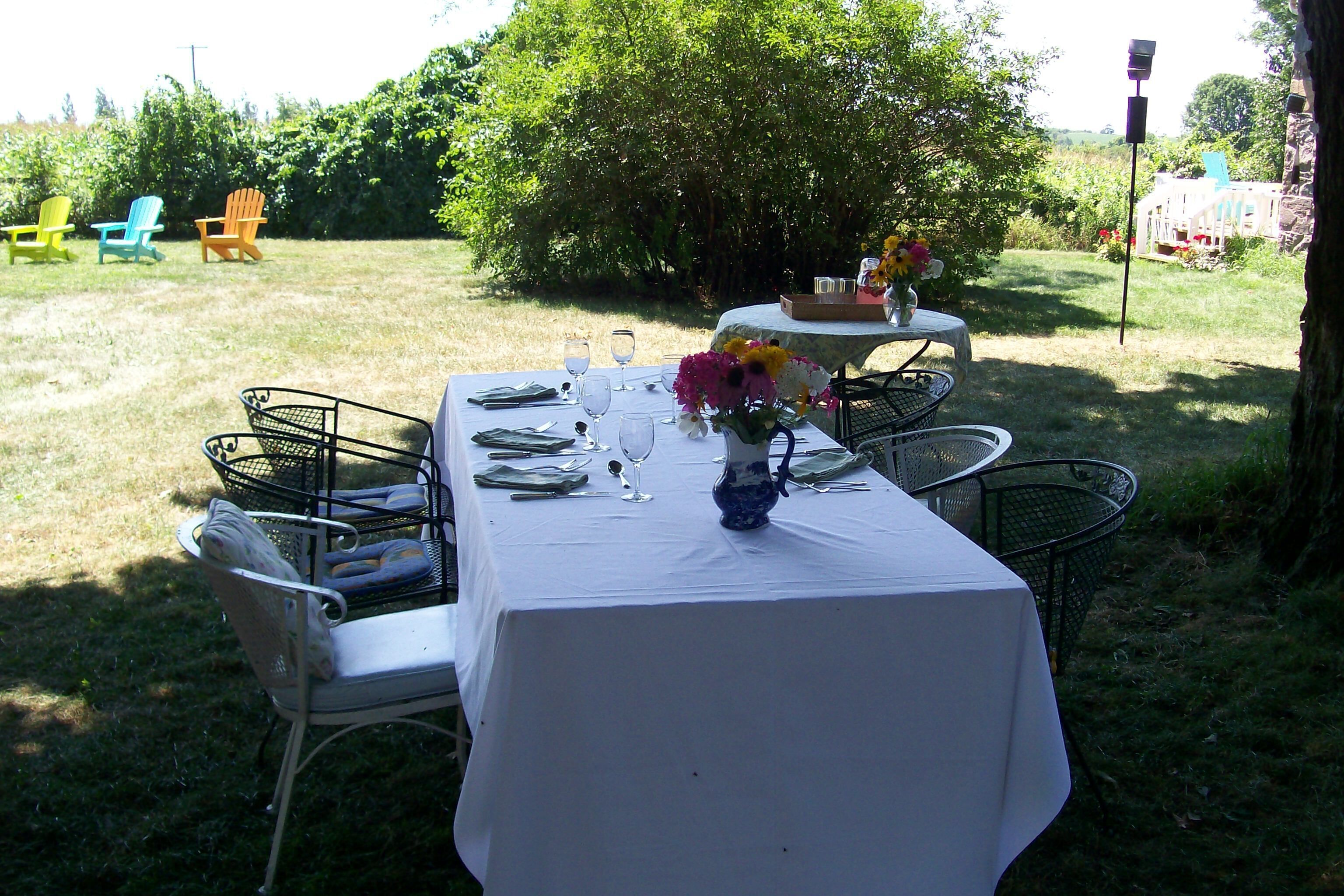 An outdoor dining area with a table set for four, surrounded by chairs, and a small table with a vase of flowers.