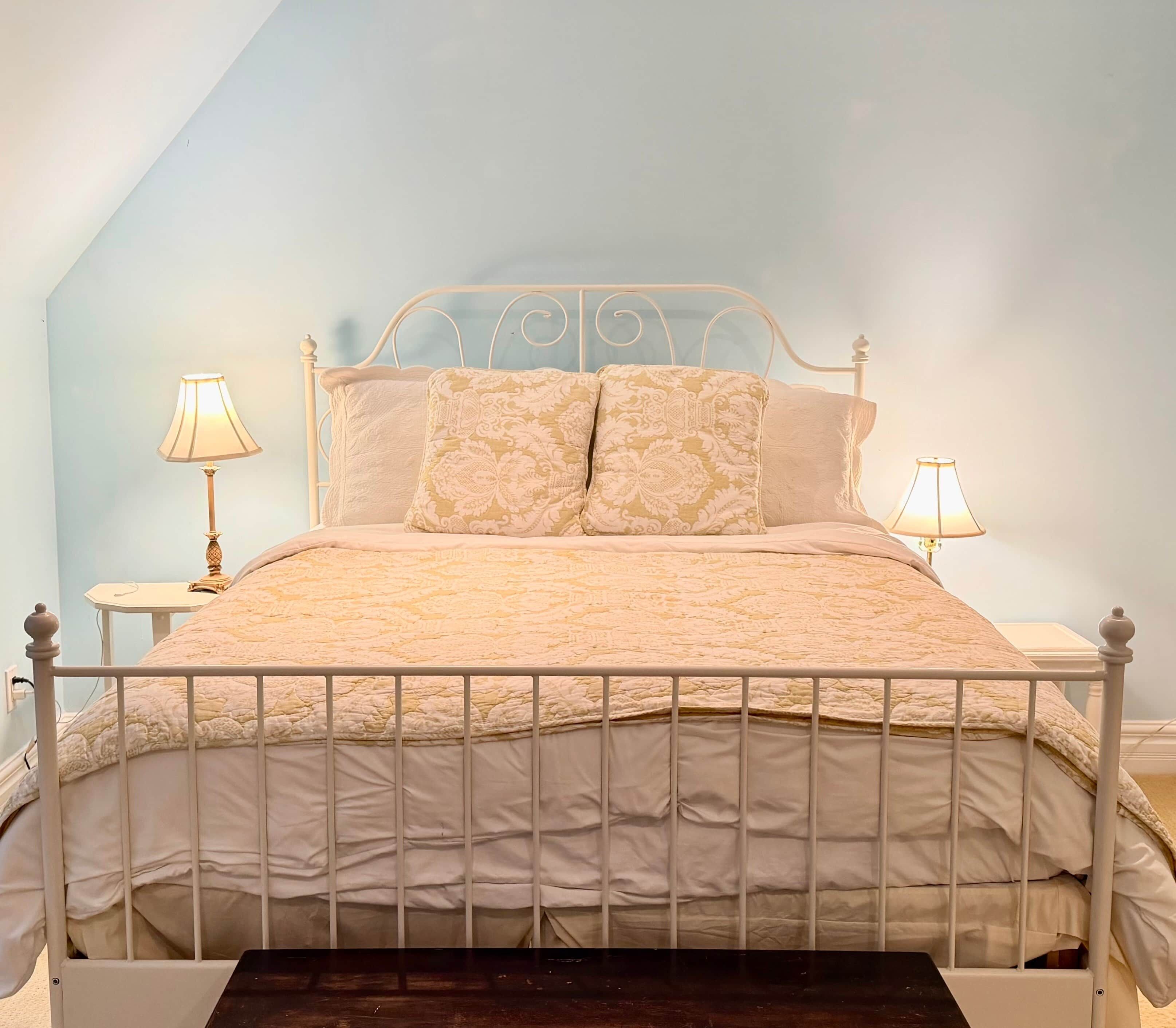 Un lit avec un cadre en métal blanc, une literie beige et deux lampes de chevet.