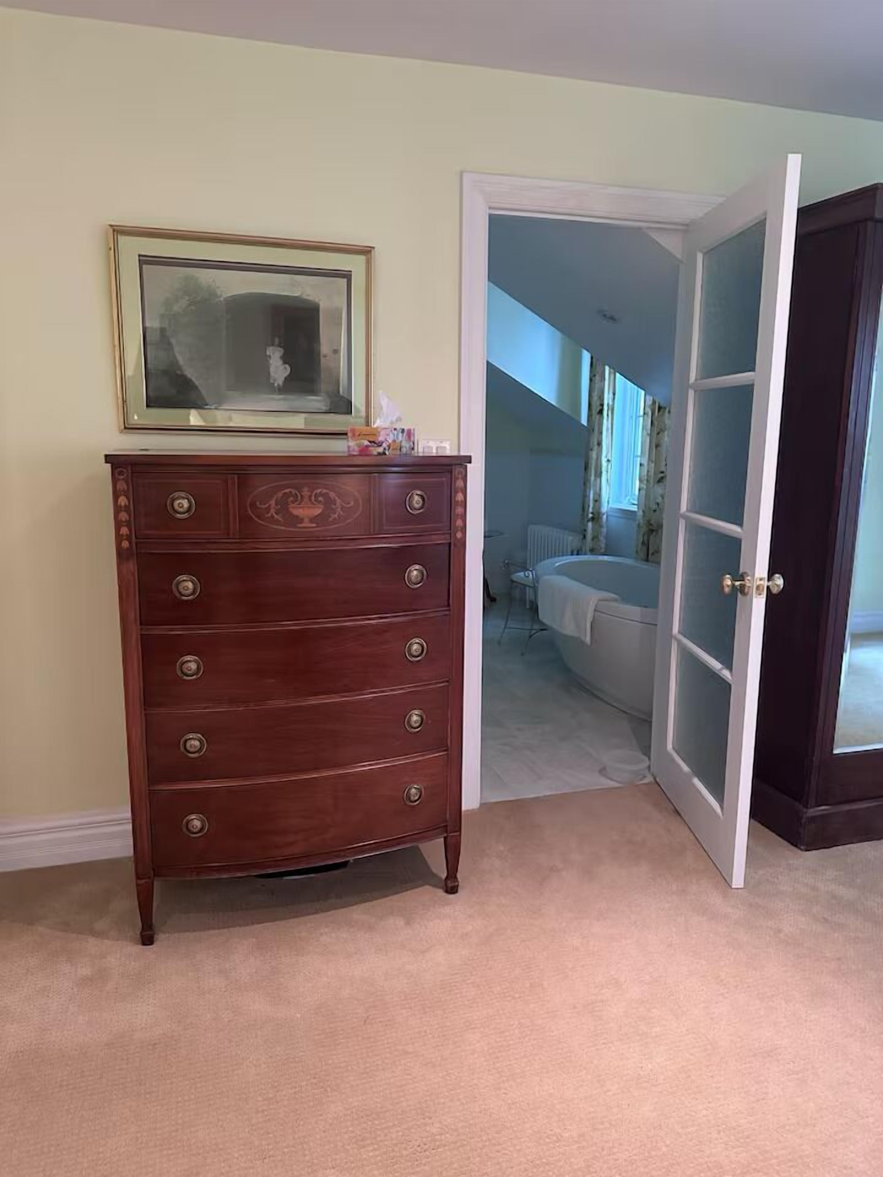 Een kamer met een houten dressoir, een lijst met een afbeelding en een deur naar een andere kamer.