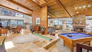 Un salón amplio con mesa de billar, techo de madera y ventanas grandes con vistas panorámicas.
