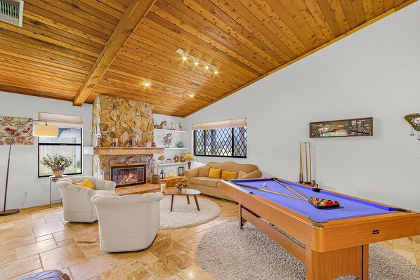 Ein gemütliches Wohnzimmer mit Billardtisch, Kamin und einer Couch.