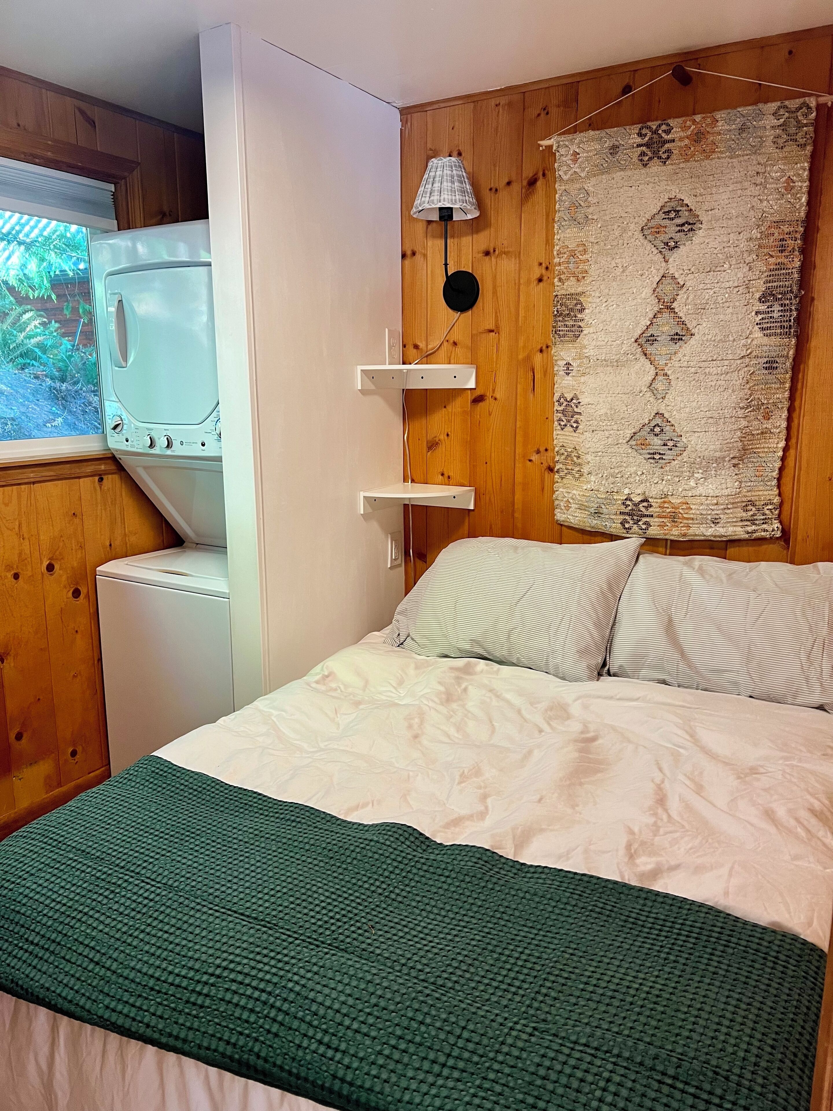 Een slaapkamer met een bed, een wasmachine, een lamp en een wanddecoratie met een patroon.