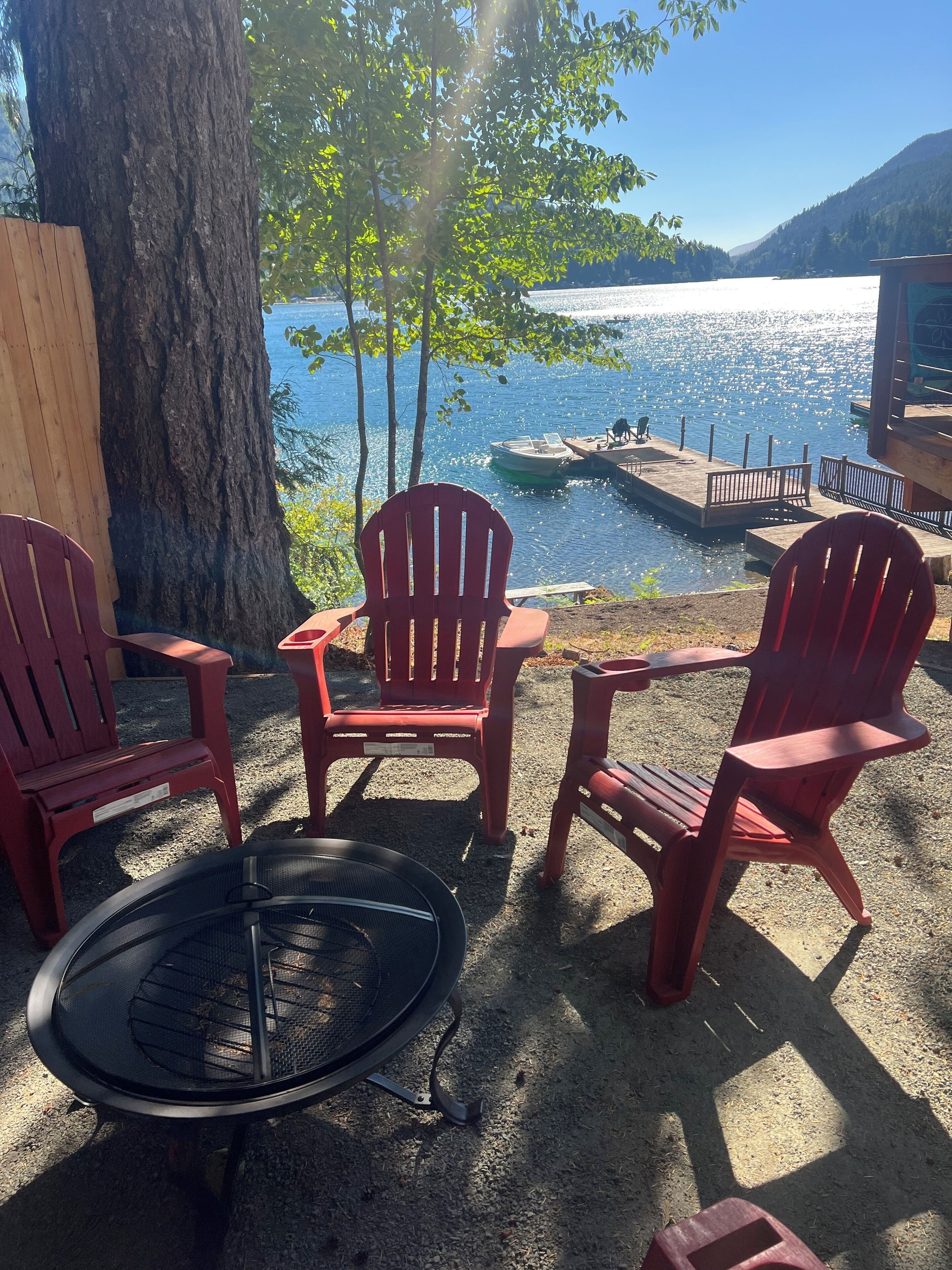 Ein Sitzbereich am Seeufer mit roten Adirondack-Stühlen, einem runden Tisch und einer Bootsanlegestelle.