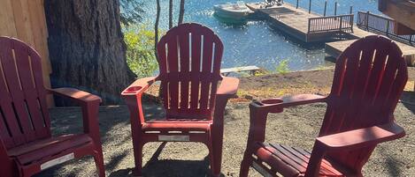 Ein Sitzbereich am Seeufer mit roten Adirondack-Stühlen, einem runden Tisch und einer Bootsanlegestelle.