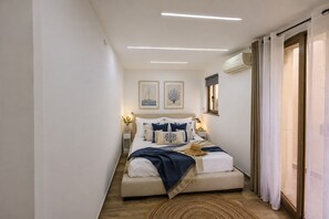 A narrow, well-lit bedroom with a bed, bedside tables, and artwork on the walls.