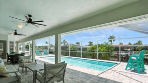 A poolside area with a pool, outdoor seating, and a view of palm trees.