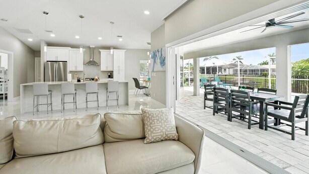 A modern kitchen with white cabinets, stainless steel appliances, and a bar area. There is a dining area with a table and chairs, and a large window overlooking a garden.