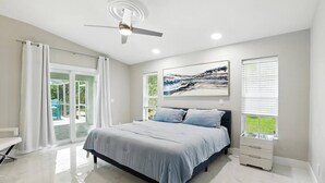 A modern bedroom with a bed, a ceiling fan, a window with blinds, and a view of the outdoors.