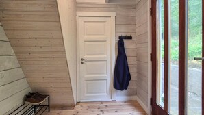 Un interior de madera con una puerta blanca, un zapatero y un abrigo colgado de un perchero.