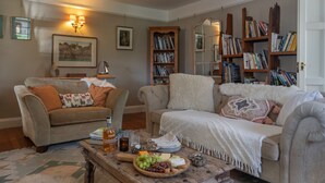 A cozy living room with two sofas, a coffee table with snacks, bookshelves, and a fireplace. - Juniper House -  a house that sleeps 17 guests  in 8 bedrooms (Kingsbridge)