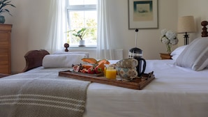 A neatly made bed with a tray of breakfast including fruits and juice, a potted plant by the window, and a lamp on the nightstand. - Juniper House -  a house that sleeps 17 guests  in 8 bedrooms (Kingsbridge)