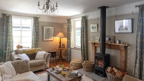 A cozy living room with a fireplace, comfortable seating, and a table with books and snacks. - Juniper House -  a house that sleeps 17 guests  in 8 bedrooms (Kingsbridge)