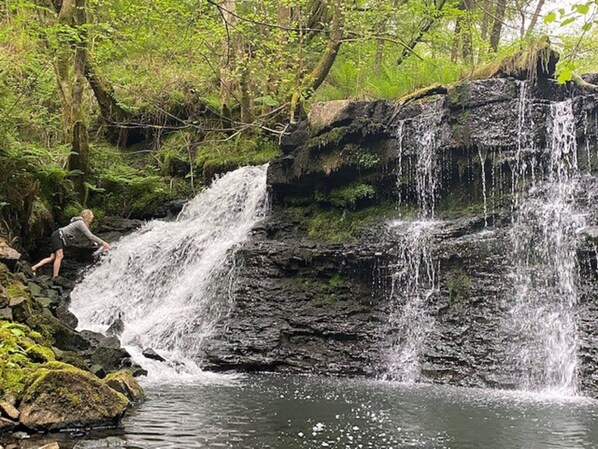 A waterfall in a forested area with a person near the water.