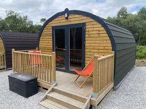 A wooden cabin with a curved roof, a glass door, and a small deck with a chair.
