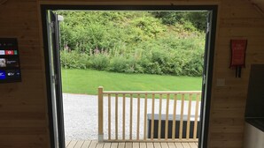 A wooden door with a welcome mat, a wooden deck, and a view of a grassy area with bushes and flowers. - A glamping pod that sleeps 2 guests  in 1 bedroom (Neath)