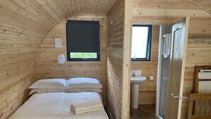 A wooden cabin room with a bed, a window, a sink, and a door. - A glamping pod that sleeps 2 guests  in 1 bedroom (Neath)