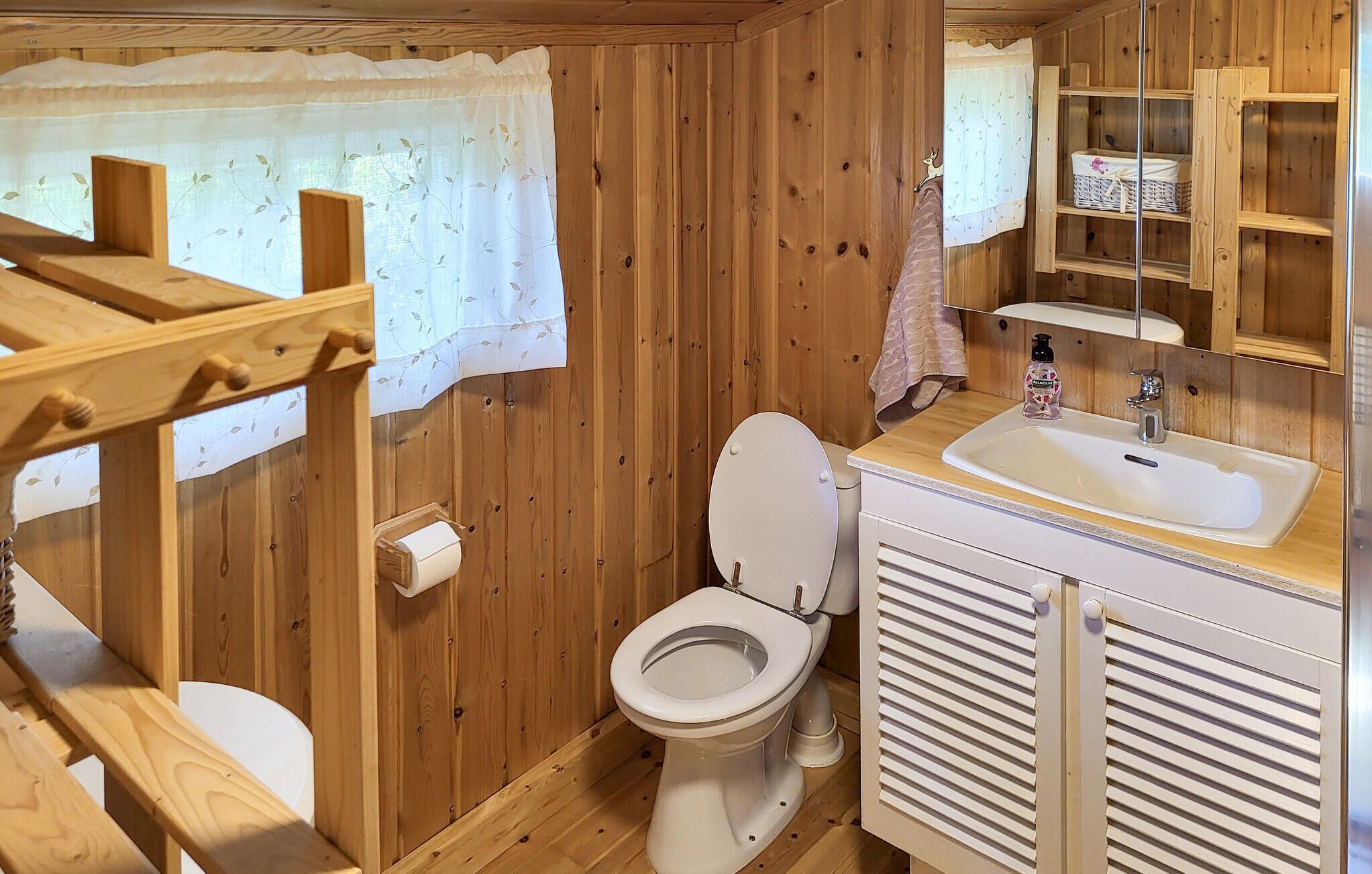 Ein Badezimmer in einer Holzhütte mit Toilette, Waschbecken und Holzregalen.