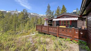 Una cabaña de madera con terraza, rodeada de árboles y montañas.