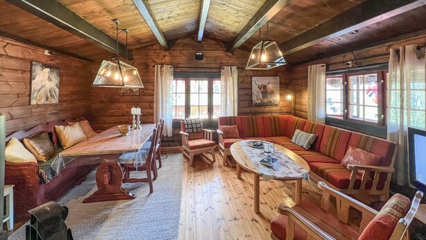 Interior acogedor de una cabaña de troncos con una mesa de comedor de madera, un sofá tapizado en rojo y una chimenea.
