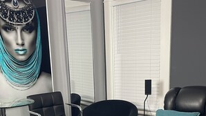 A modern living room with a black leather sofa, a black armchair, a glass table, and a blue accent pillow.