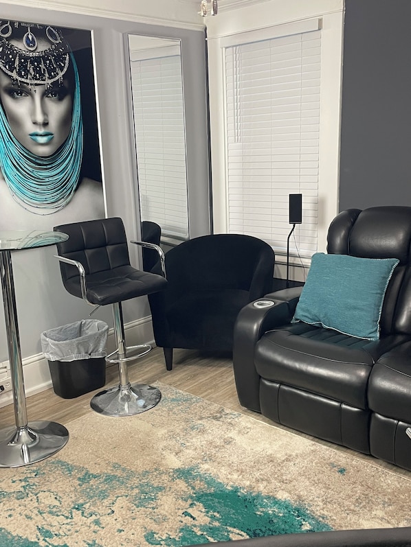 Ein modernes Wohnzimmer mit einem schwarzen Ledersofa, einem schwarzen Sessel, einem Glastisch und einem blauen Zierkissen.