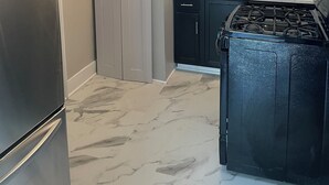A kitchen with dark cabinets, a stainless steel refrigerator, a gas stove, and a tiled backsplash.