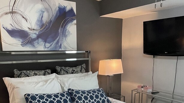 A modern hotel room with a large bed, a ceiling fan, a flat-screen TV, and a large abstract painting on the wall.